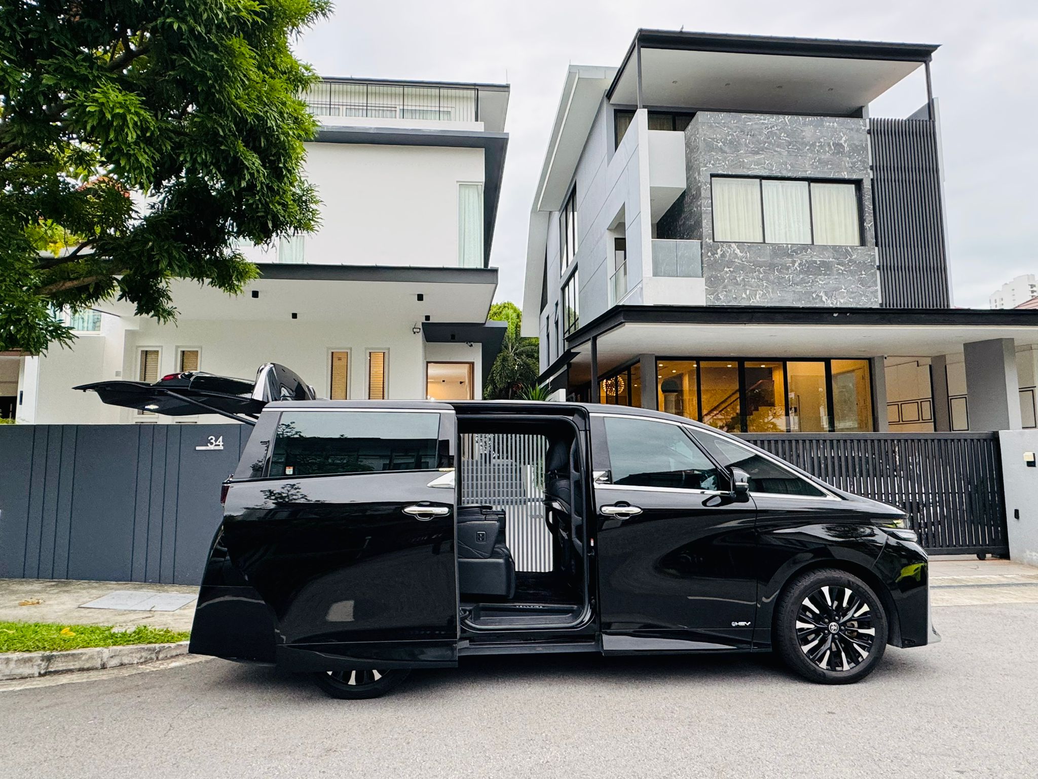 A sleek black luxury van with doors open, ready for passengers, parked in front of modern, luxurious homes, highlighting a premium chauffeur service