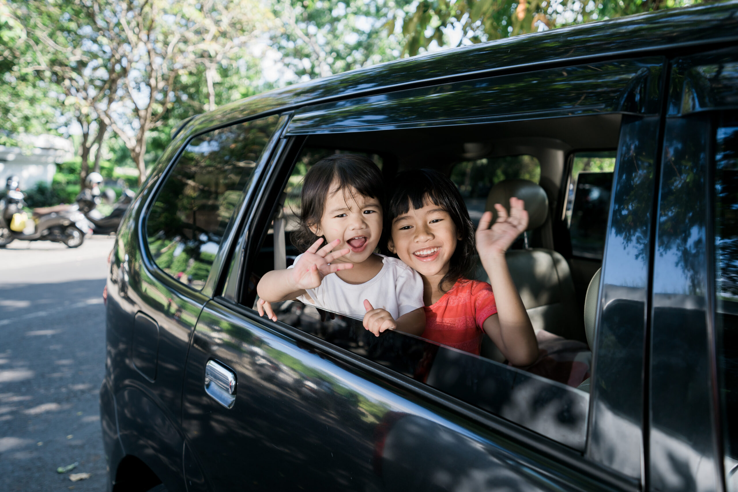 Kids smiling and waving while traveling in a car