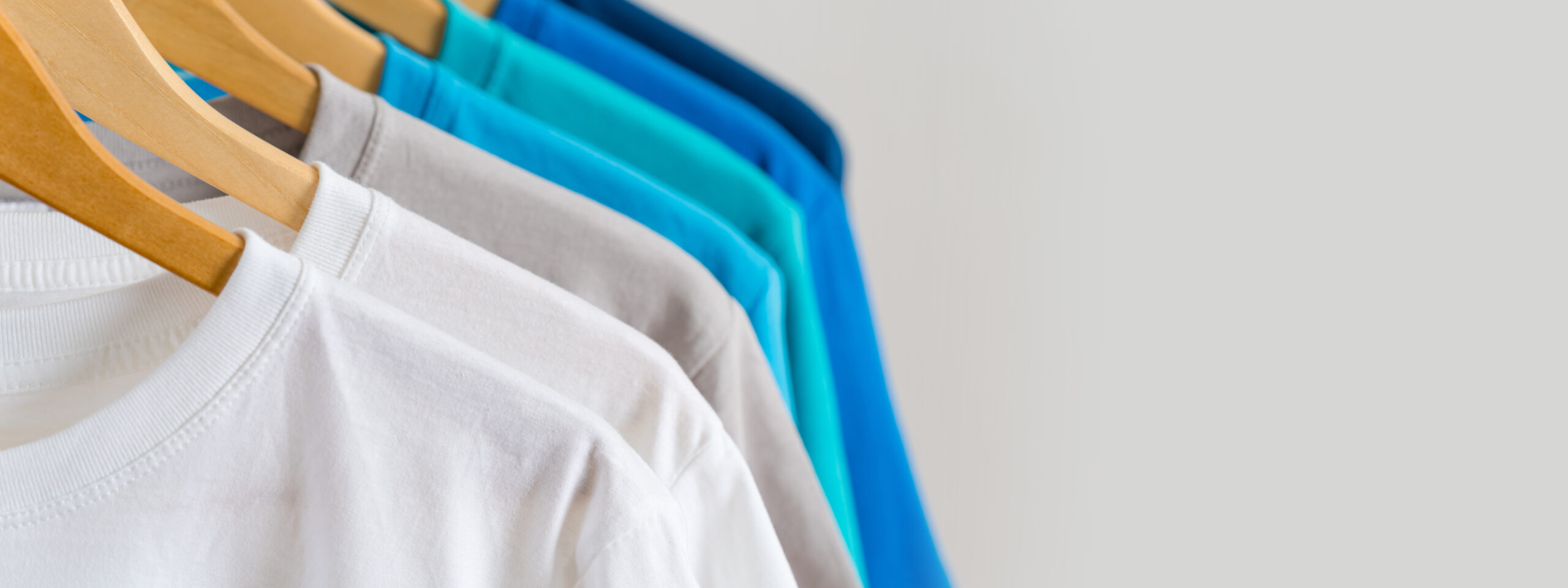 A close-up of several t-shirts on wooden hangers