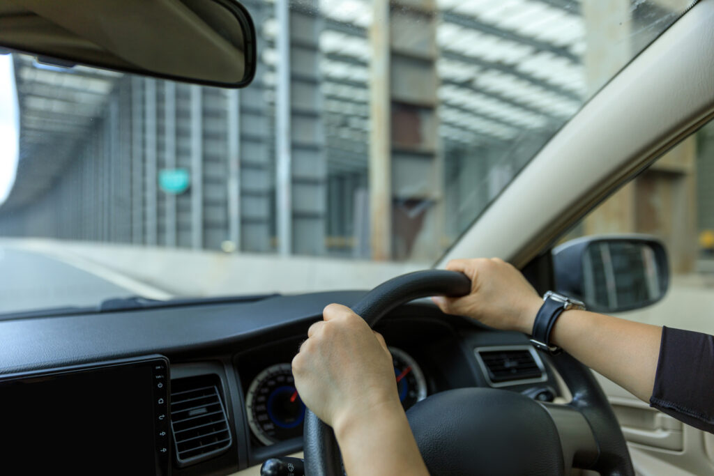 Driver's perspective view showing hands gripping the steering wheel while driving a car on a road