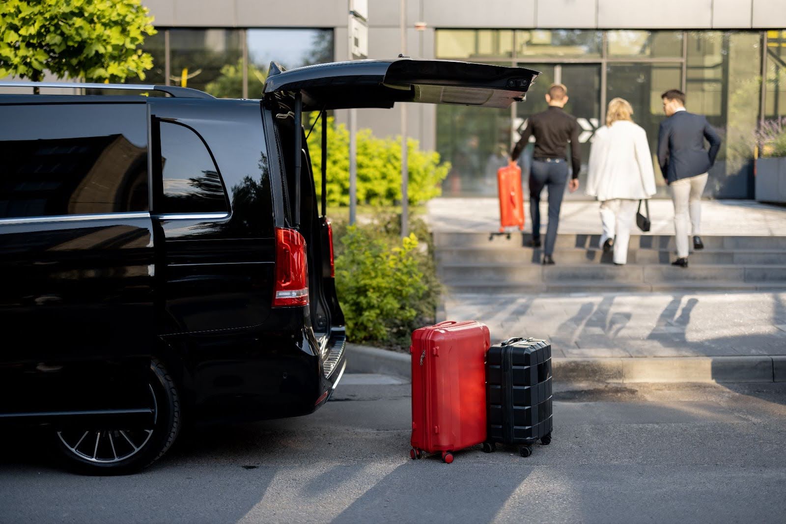 Black luxury van with an open trunk and luggage on the pavement, ready for airport transfer.